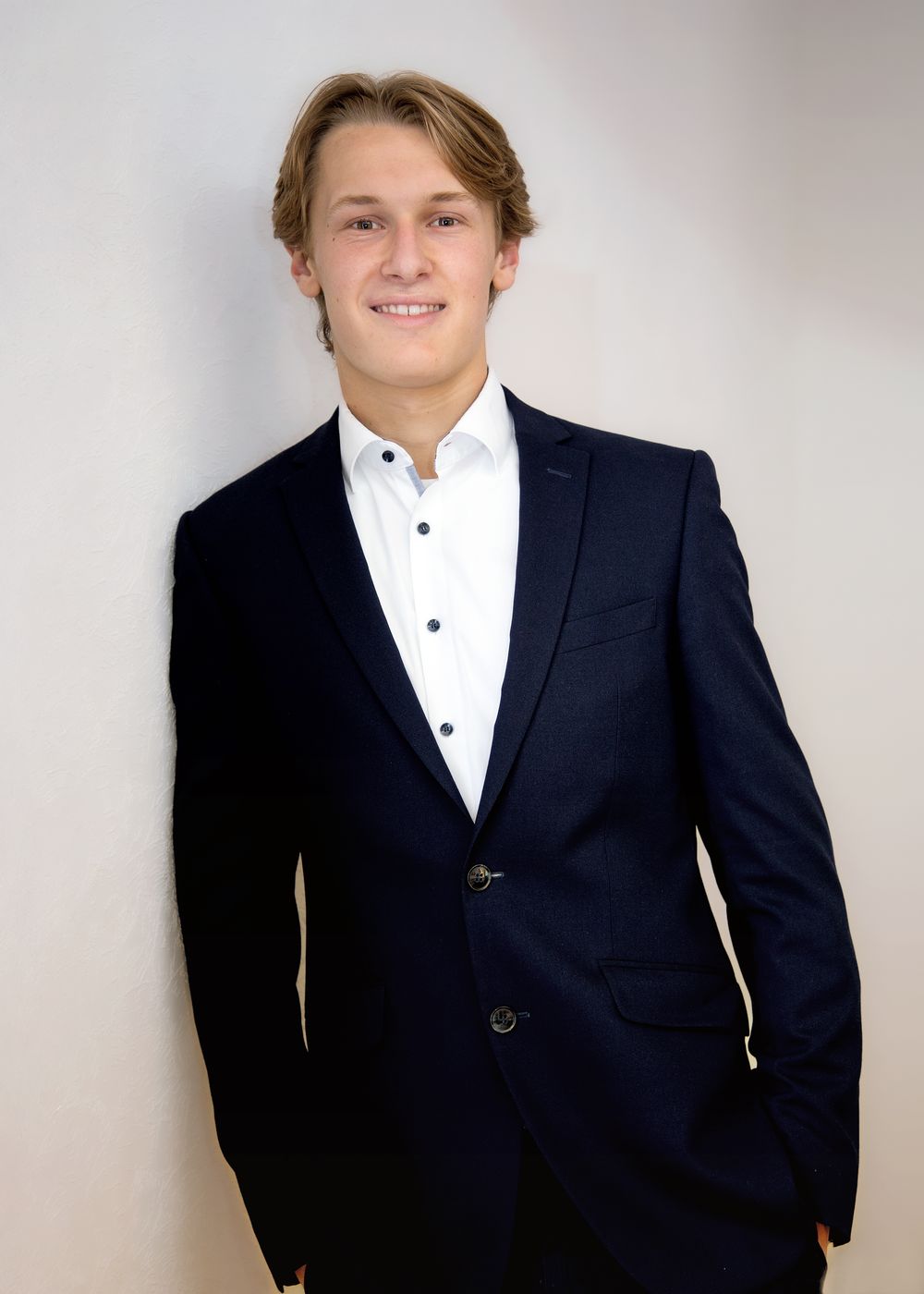 Young man in navy suit and white dress shirt smiling confidently against a light gray background. Bewerbungsfoto modern, zeitlos, klassisch