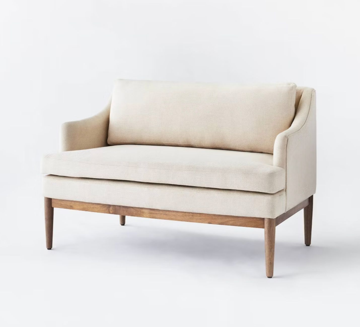 Modern beige upholstered settee with curved back and wooden base featuring clean lines and minimalist design.
