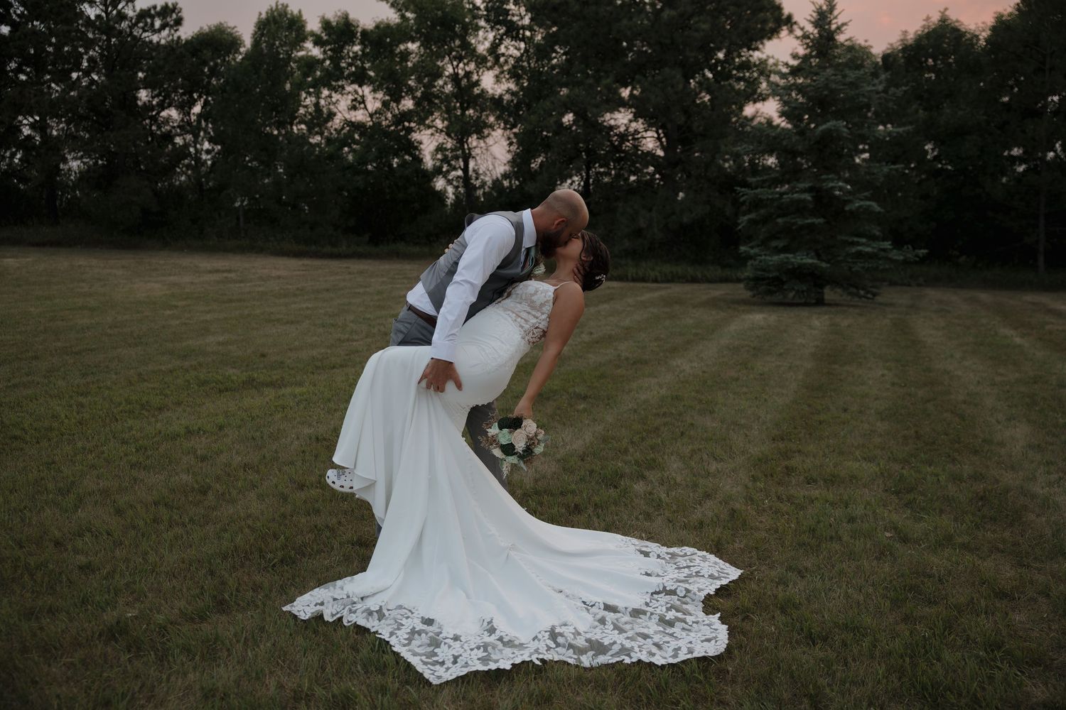 Bride and groom embrace near a reflective mountain stream in Bismarck, ND with the mountain peaks in the background.
