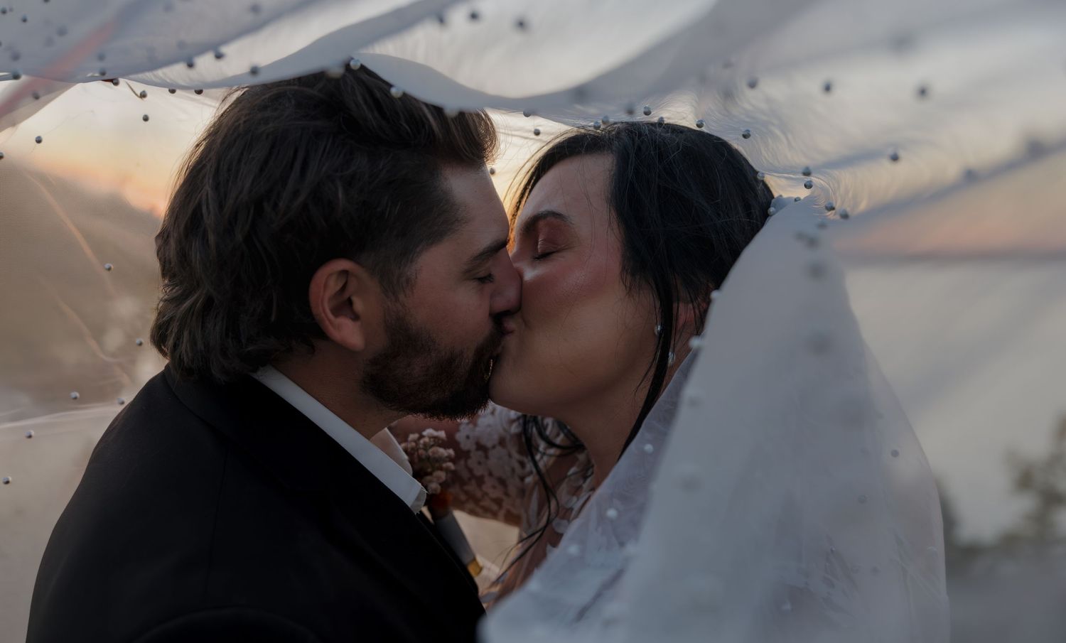 Bride and groom embrace near a reflective mountain stream in Bismarck, ND with the mountain peaks in the background.