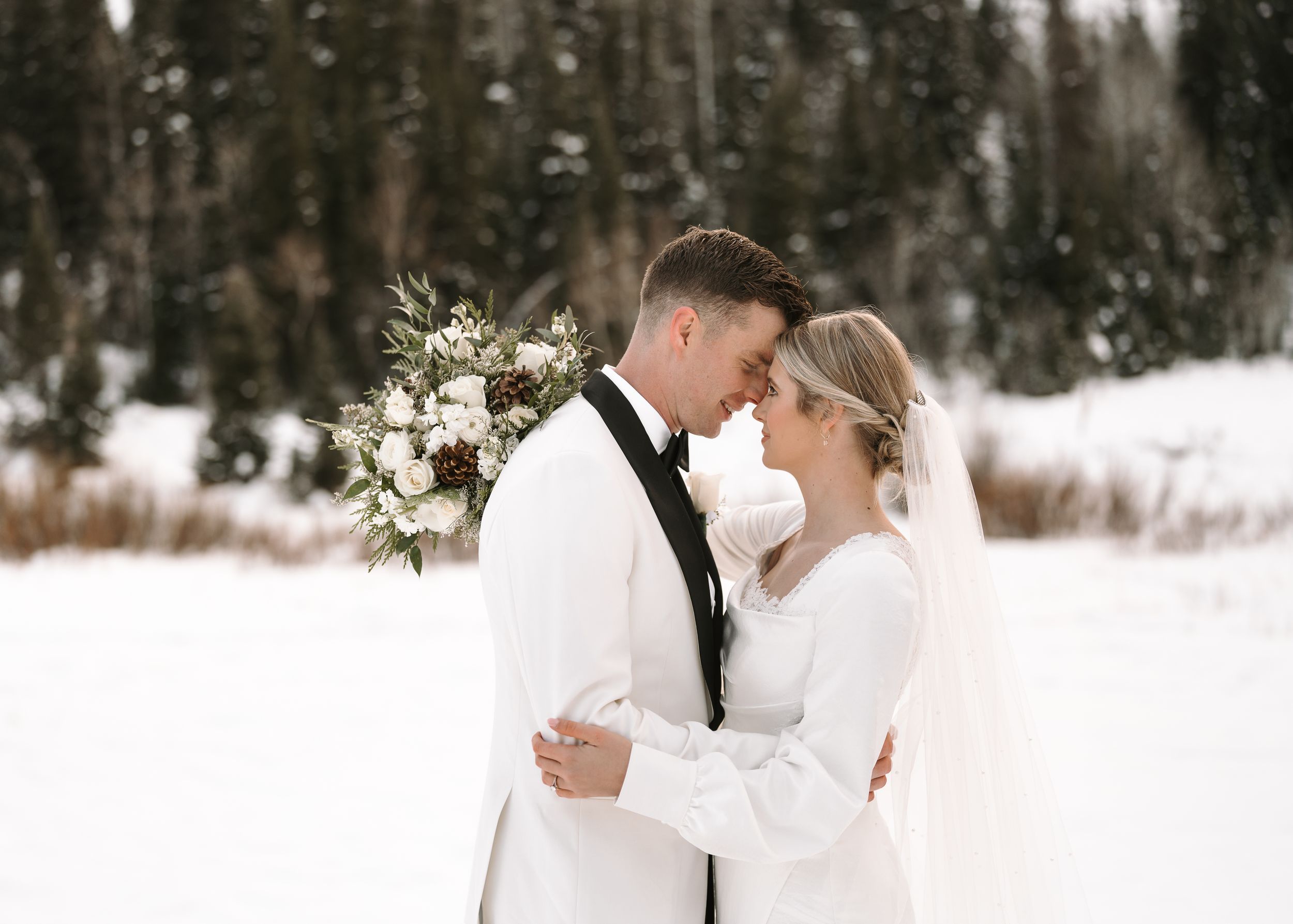 A romantic winter wedding scene with a couple embracing amid snowy scenery and bare winter trees.