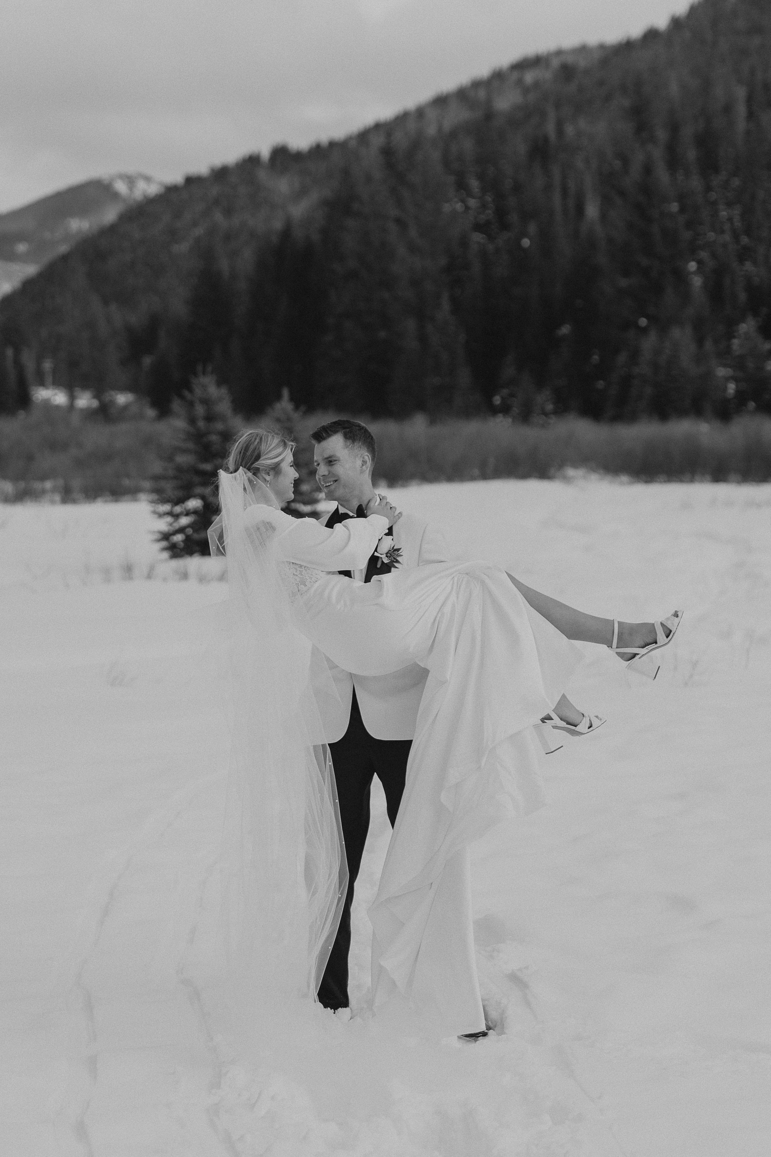A romantic outdoor winter engagement session in black and white showing the couple dancing in fresh snow.