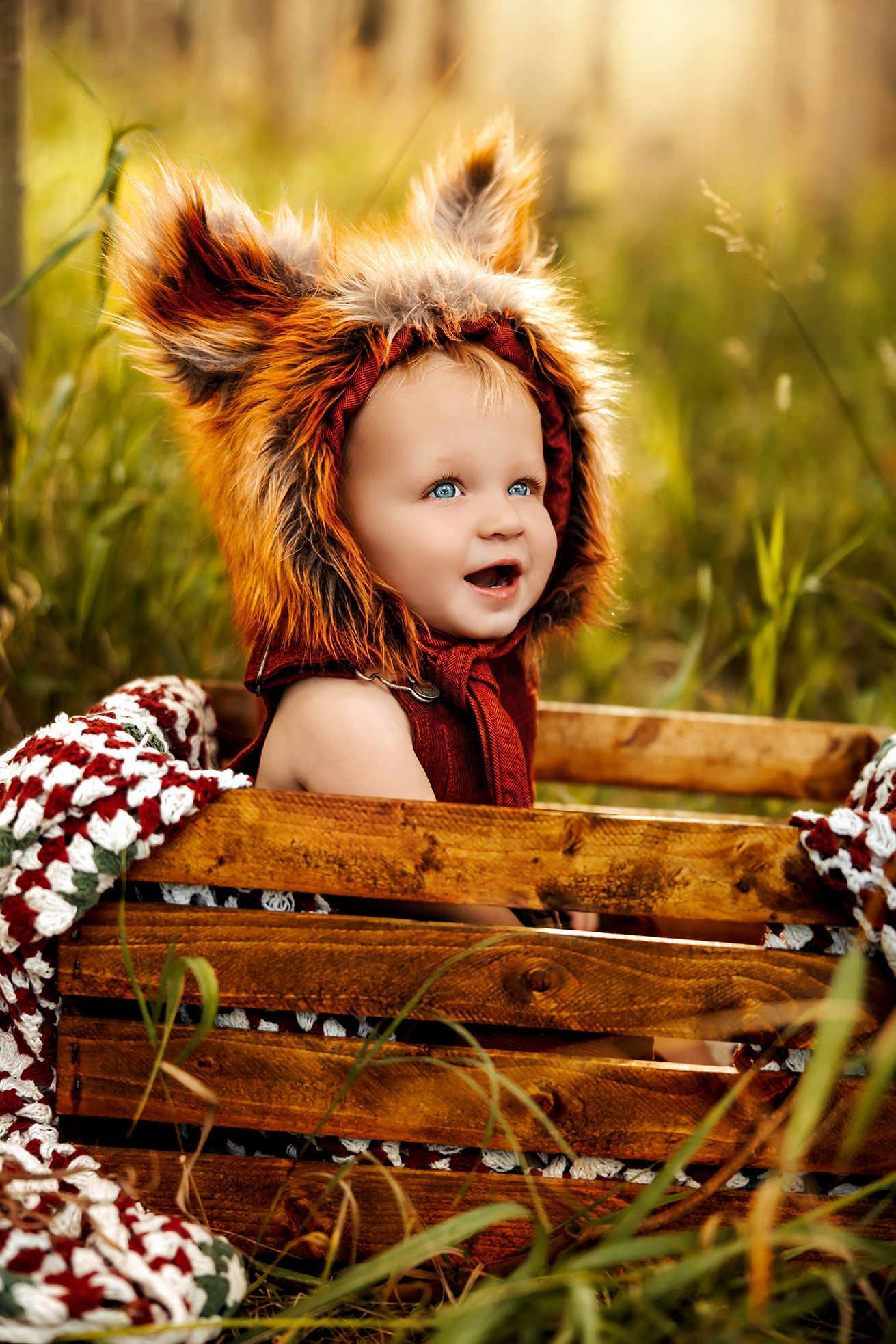 A child in a furry fox hood sits in a wooden crate among tall grass during golden hour. pueblo colorado photographer