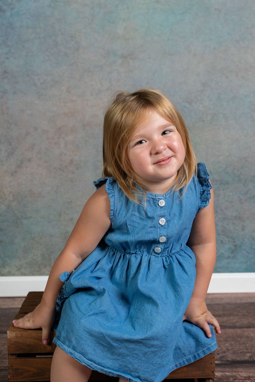 A series of candid expressions while sitting on a wooden surface wearing a blue denim dress.