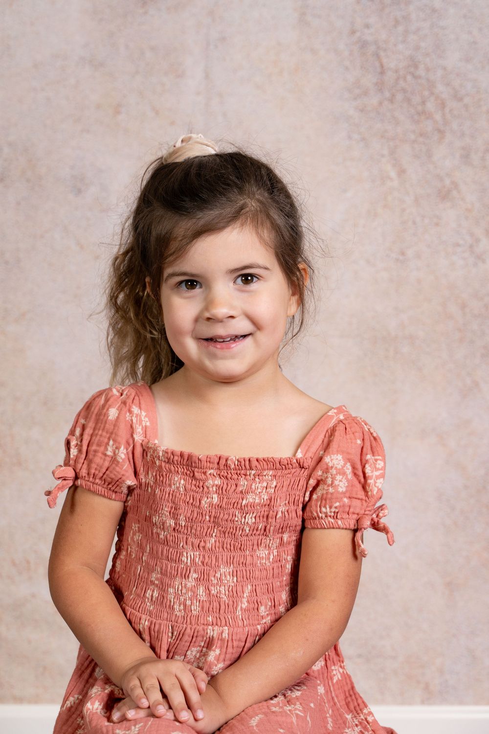 A series of portrait photos showing a young child in a coral-colored smocked dress against a neutral backdrop.