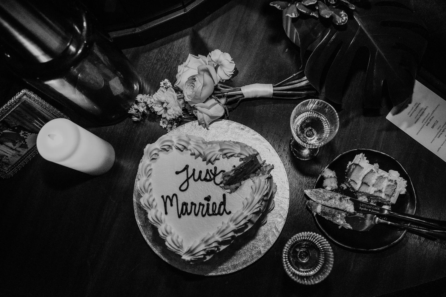 Black and white overhead shot of Just Married cake with champagne glasses and flowers.