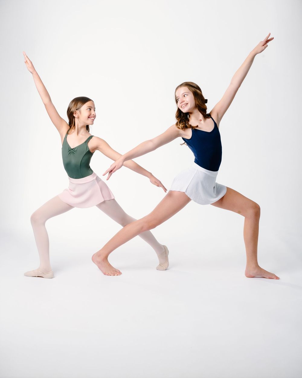 Dancers in leotards perform a series of graceful lunging poses against a white backdrop in a contemporary dance studio.