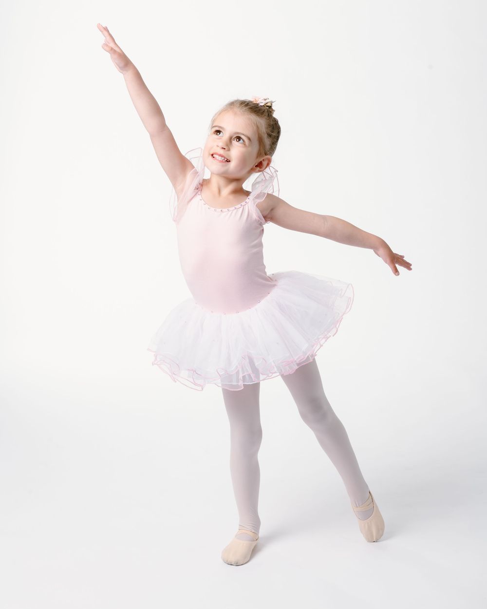 Young ballet dancer in pink leotard and white tutu strikes a graceful pose against white background.