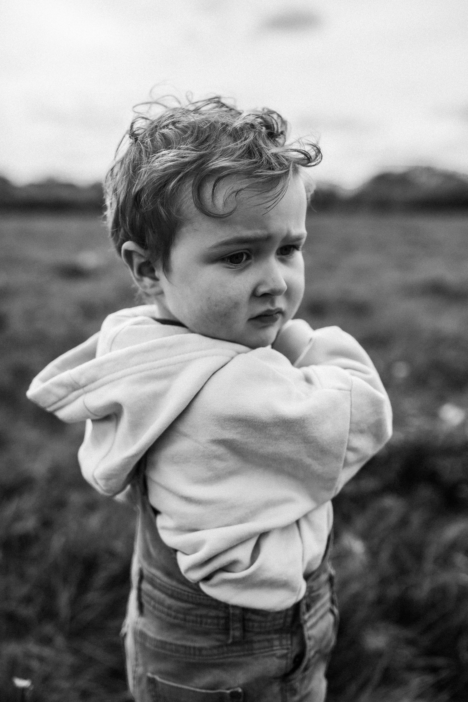 A portrait of a young child in a light hoodie looking away dramatically in black and white.