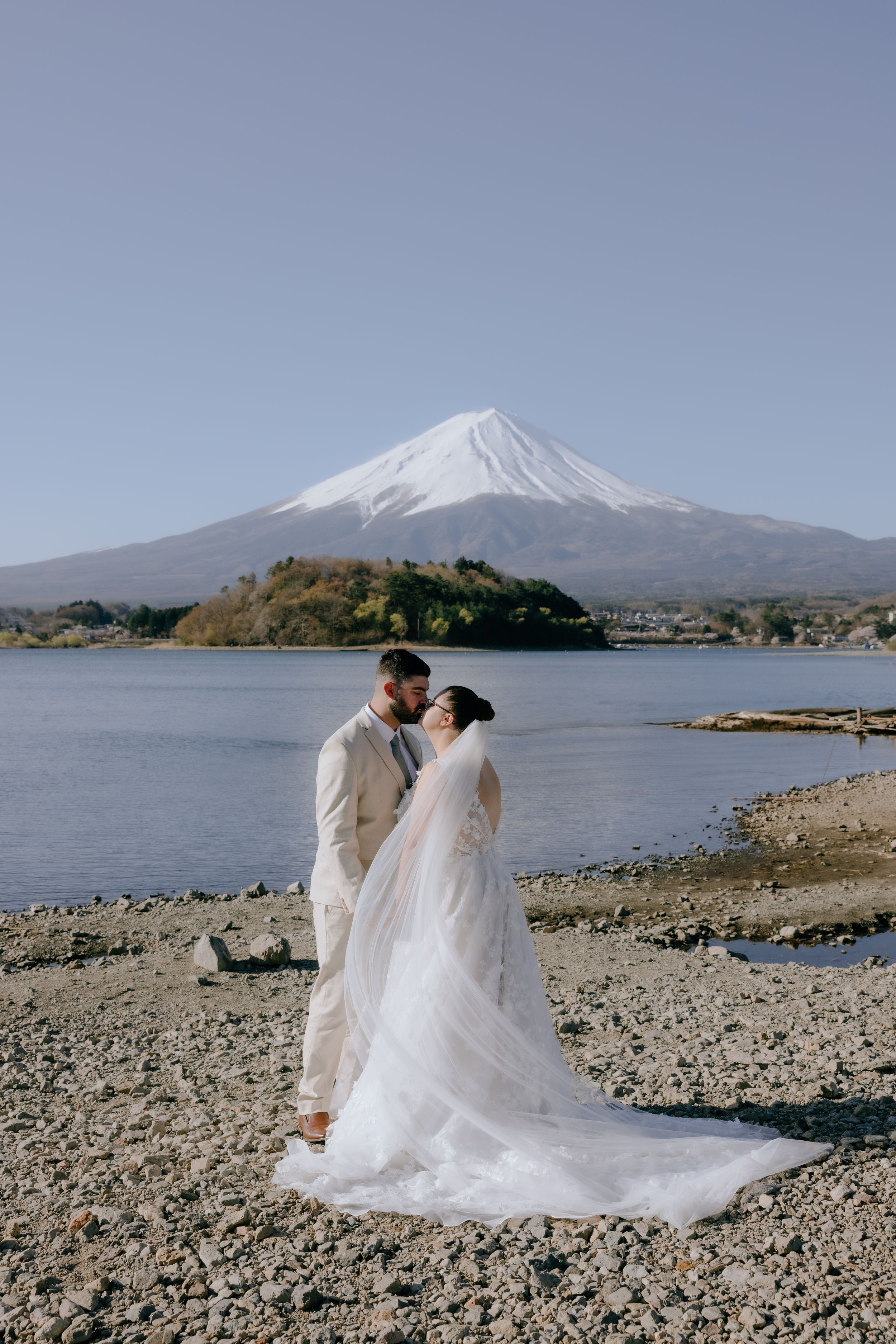 A couple in wedding attire shares a romantic moment with Mount Fuji and Lake Kawaguchiko as their majestic backdrop in Japan.