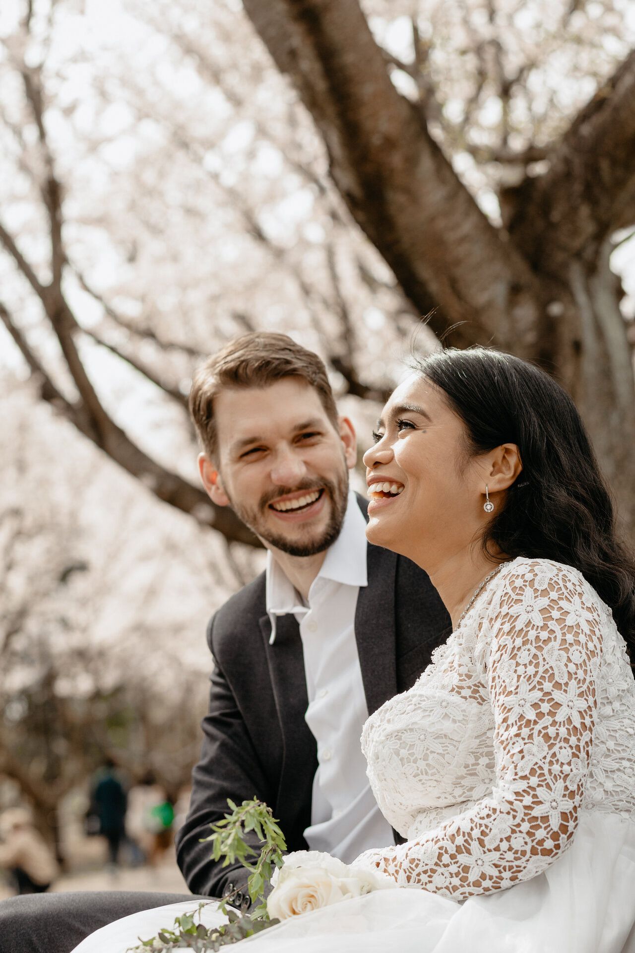 A joyful couple in wedding attire share a candid laughing moment outdoors.