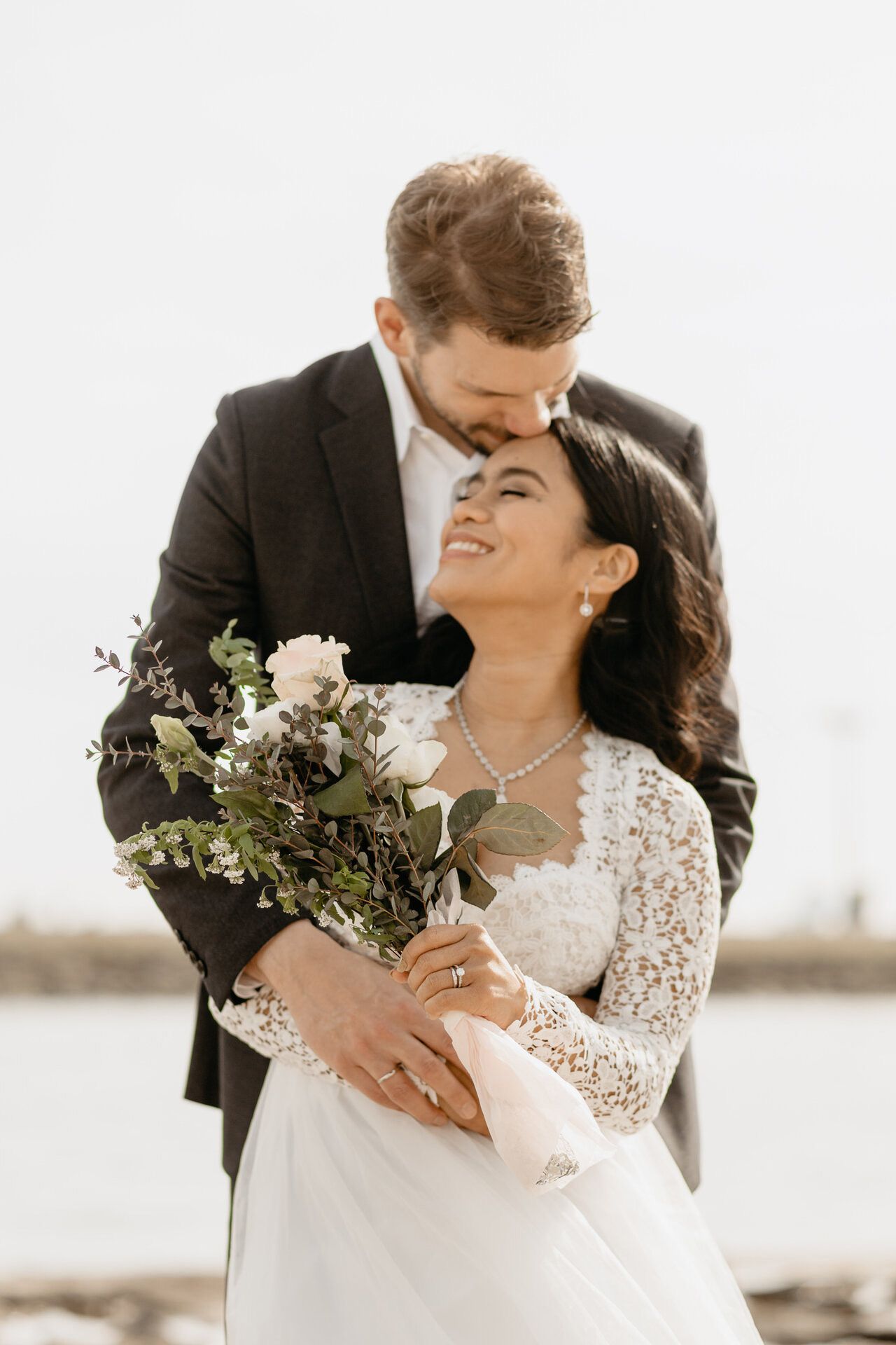 An intimate moment between newlyweds with a white floral bouquet and lace dress.