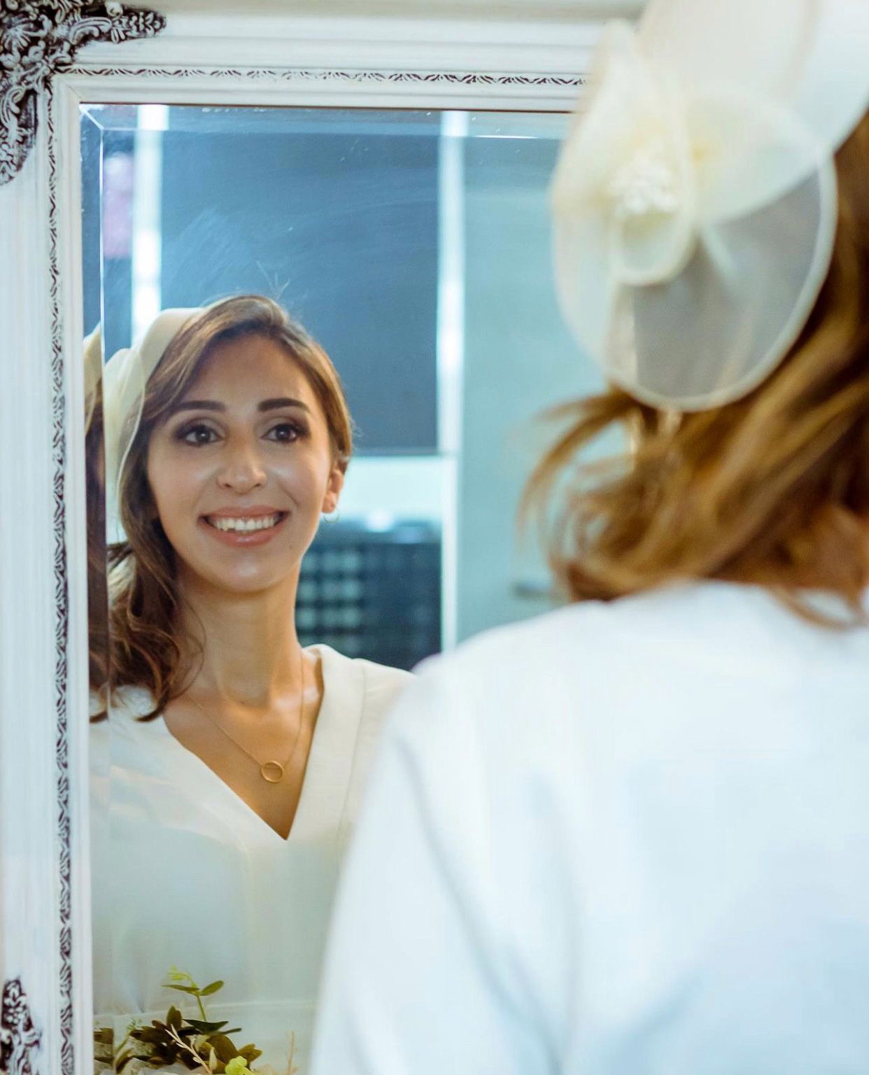 Reflection of bride in ornate vintage mirror during wedding preparations.
