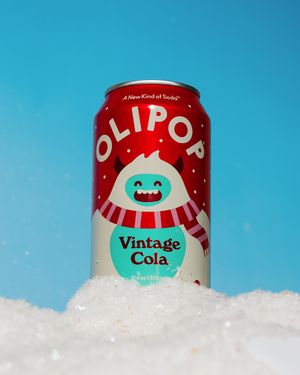 Picture of Olipop Vintage Cola Can. A red can with a white yeti and the word "Olipop" in white across. The can is sitting in fake snow.