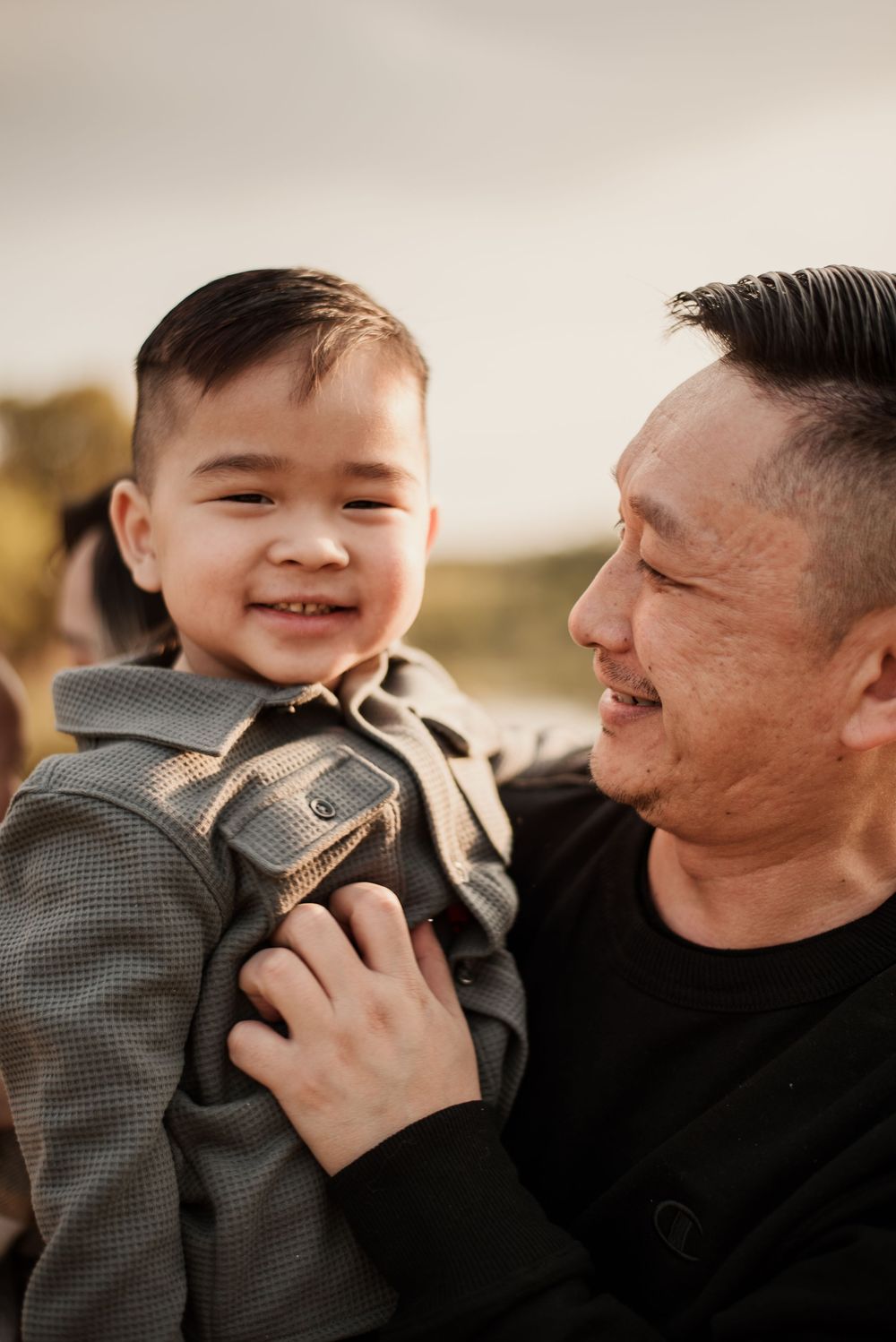 A smiling young boy being held by a man, sharing a joyful moment outdoors in warm light.