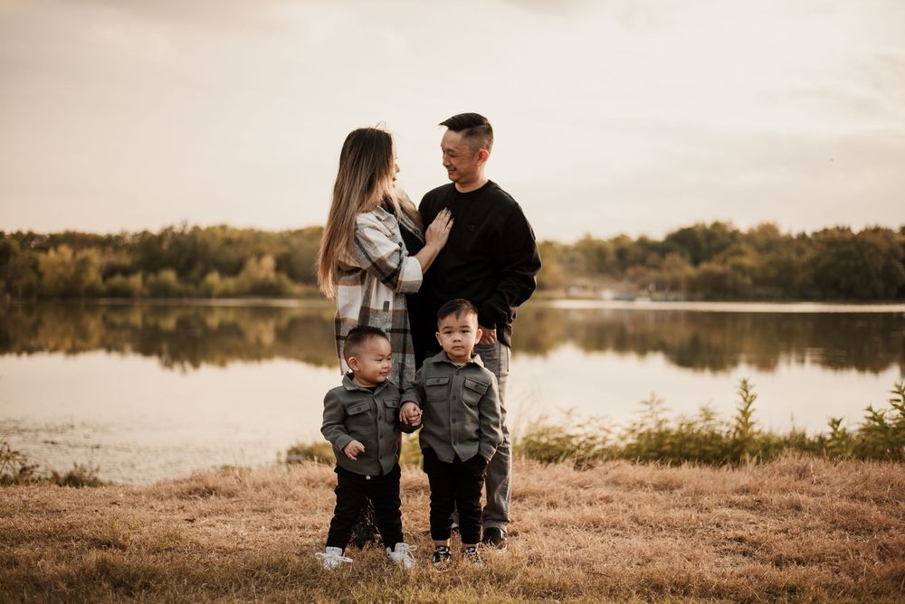 Family of four posing by a lake during golden hour, parents gazing at each other with two young children standing in front.