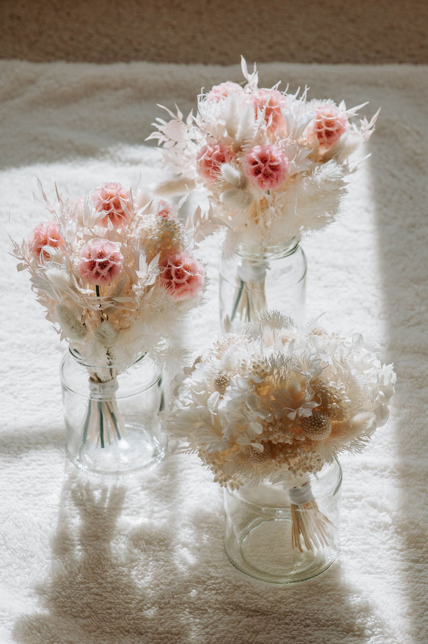 Delicate pink and white dried flower arrangements in clear glass vases on white surface.