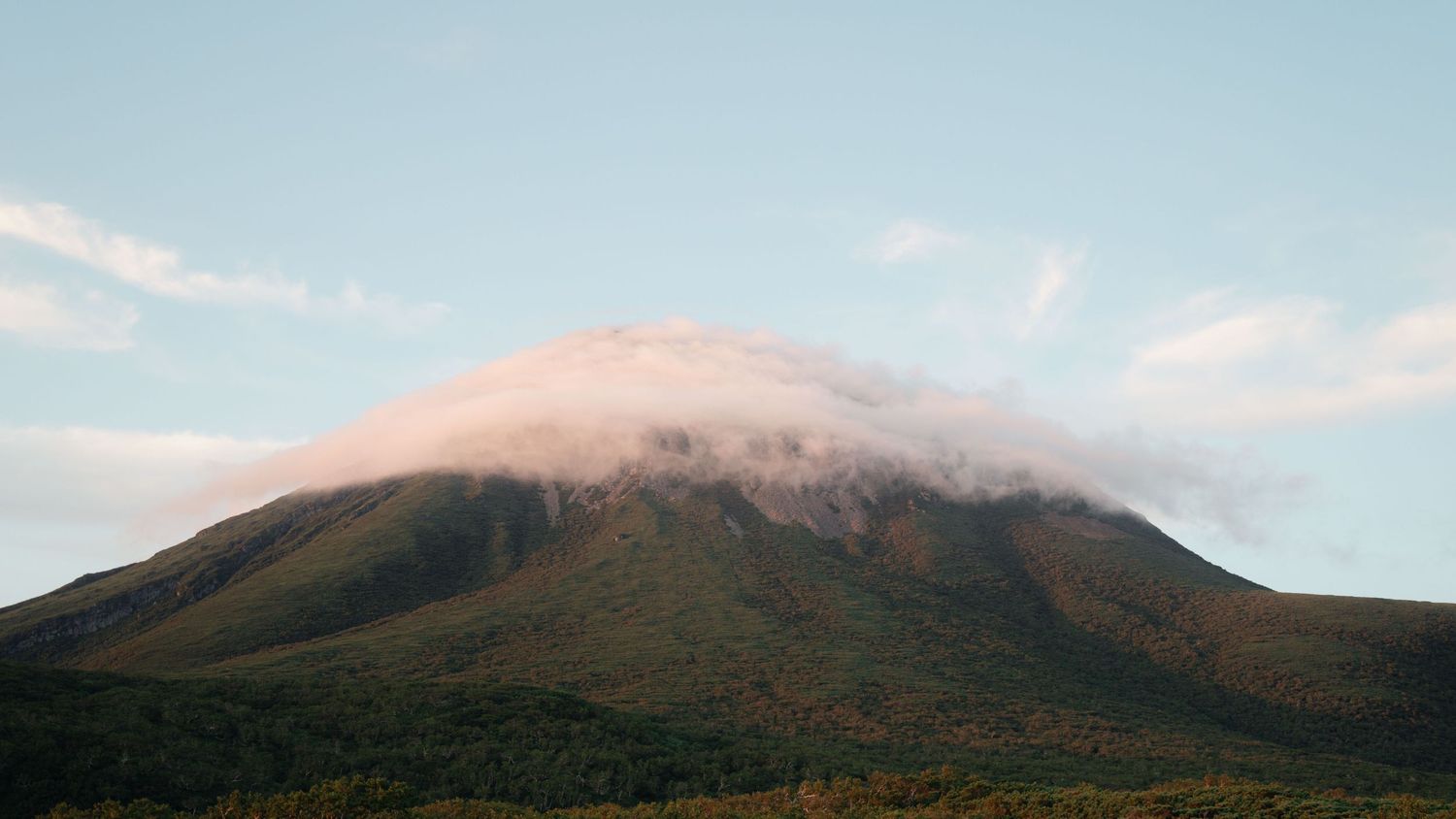 Majestic mountain peak with clouds wrapping around its summit against a blue sky.