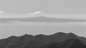Distant mountain range silhouetted in black and white with clouds floating above.