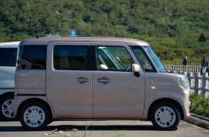 Light pink compact van parked in a lot with a blue sign visible.