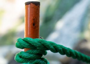 Green rope tied around an orange metal pole in close-up detail.