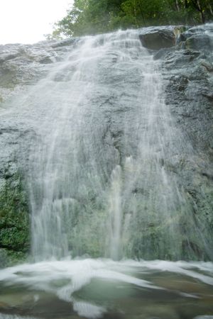 Wide waterfall flowing down a grey rock face creating a misty cascade.