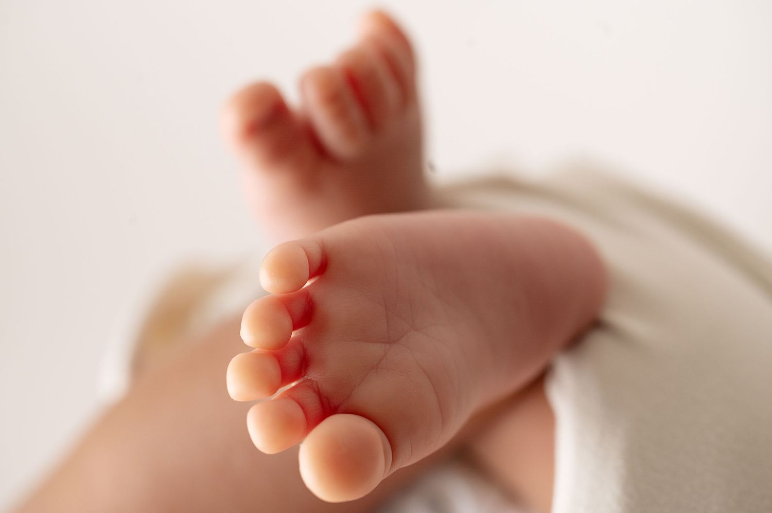 Close-up of tiny newborn baby foot against white background showing delicate toes.
