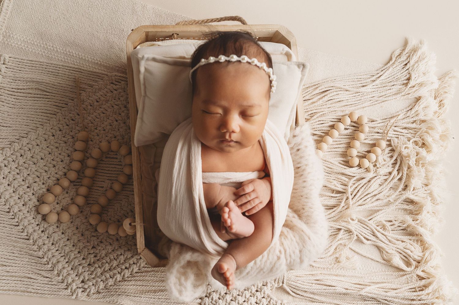 Newborn baby with headband sleeping in wooden crate with textured macrame decor.