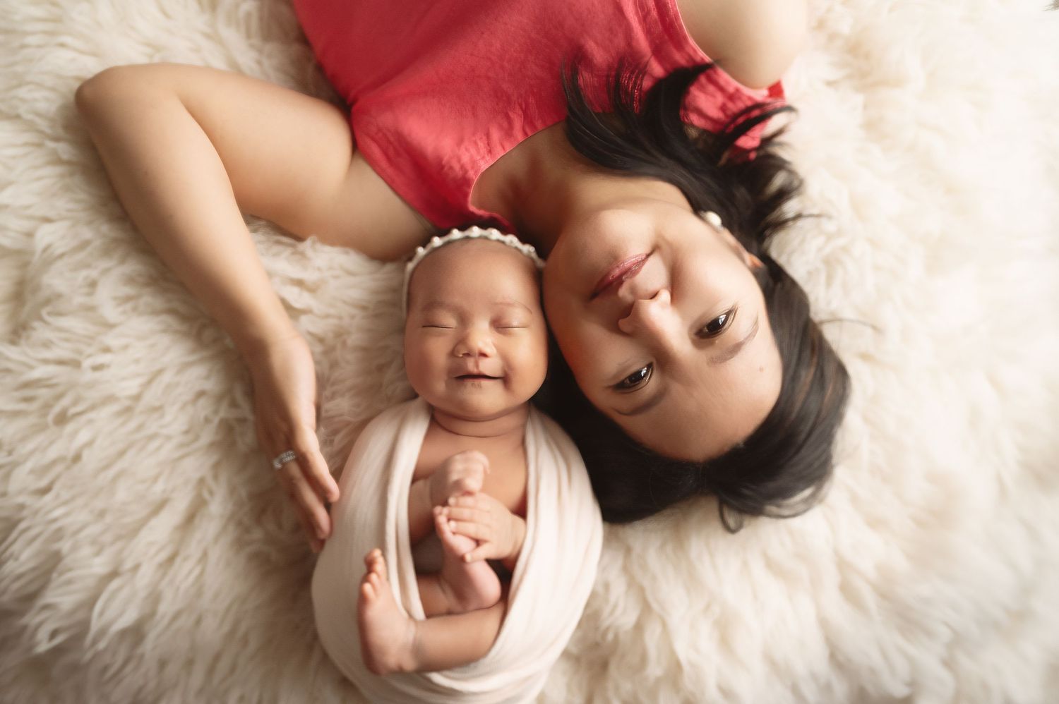 Mother and newborn lying on white fur blanket in studio portrait setting.