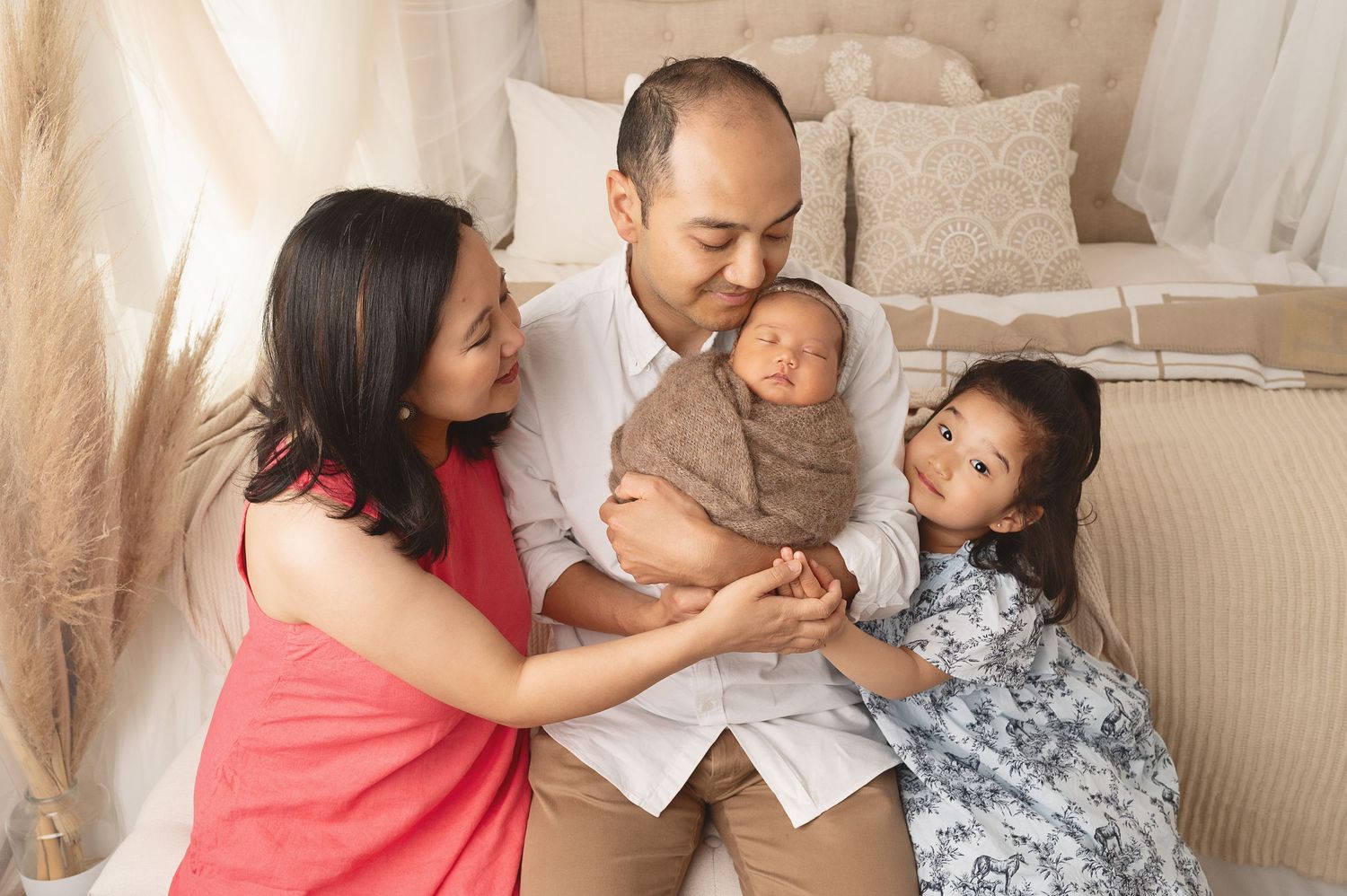 Family gathered on couch sharing tender moment with newborn and young sibling.