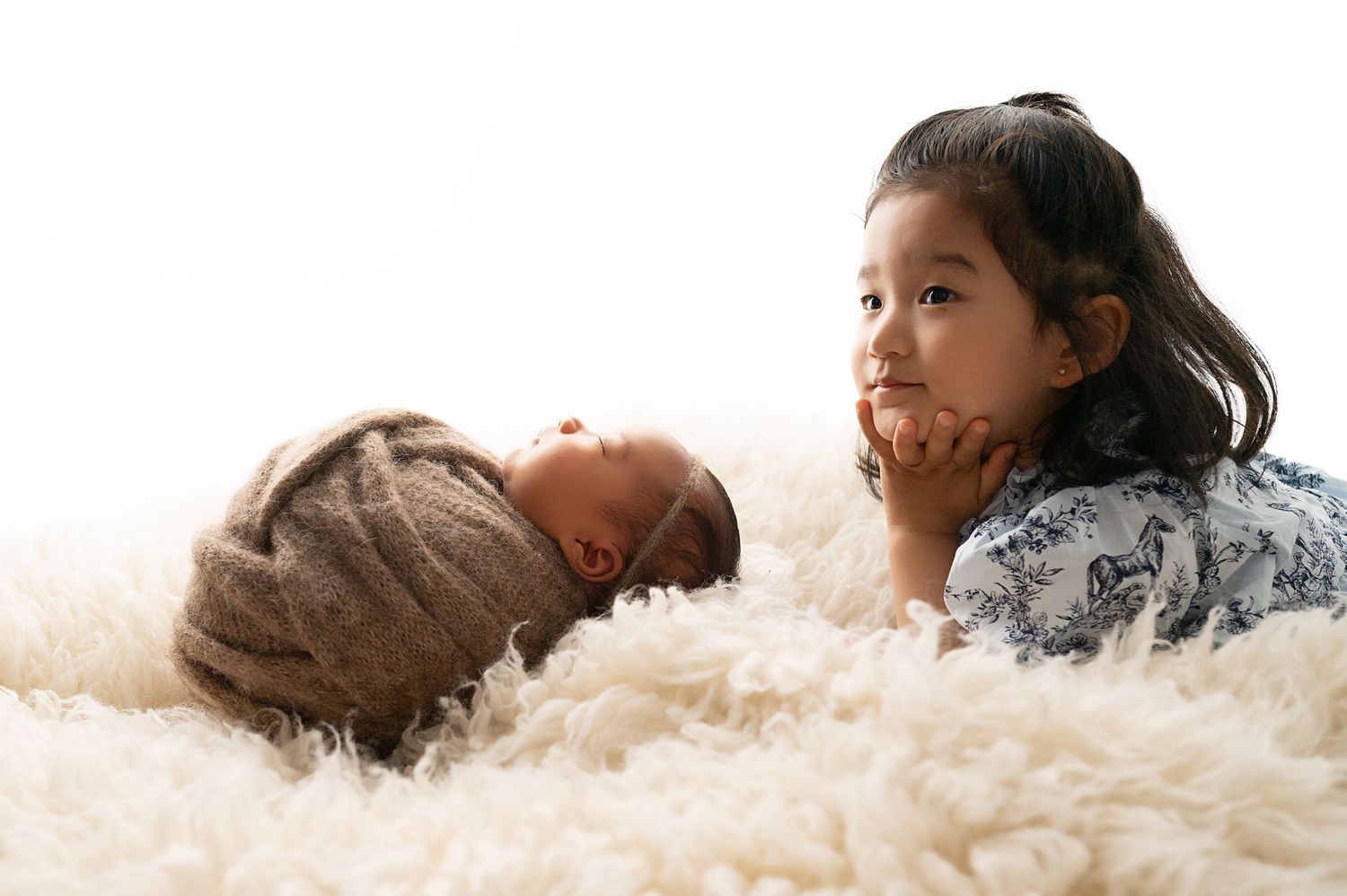 Sweet siblings lying on fluffy white rug during photo session.