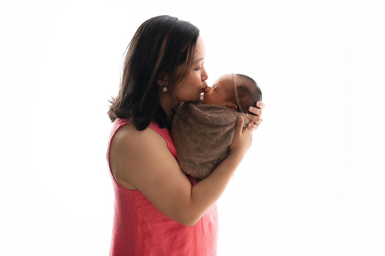 Tender moment between parent and swaddled newborn in studio portrait.