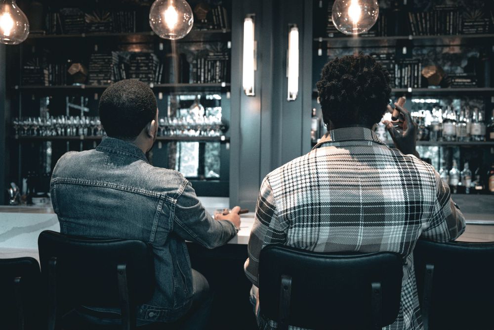 Dimly lit bar interior with illuminated pendant lights and patrons seated at tables.
