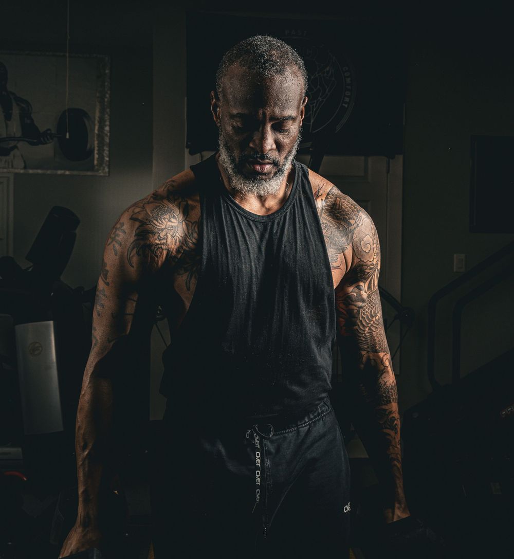 Dark moody portrait showing tattooed arms in dramatic lighting.