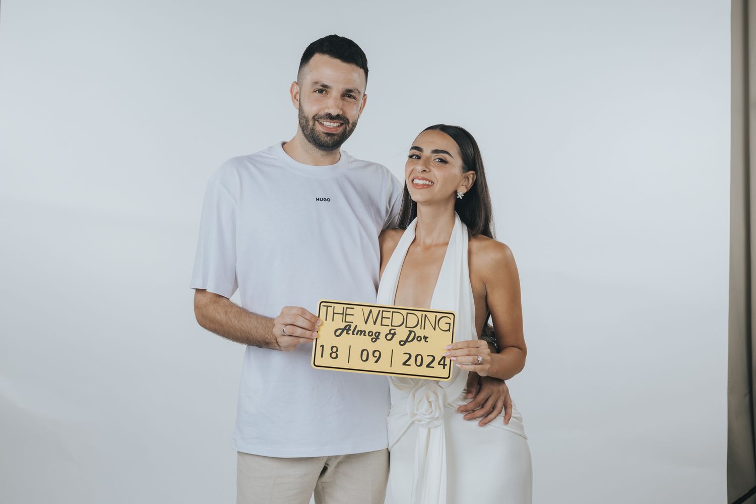 Couple holding a dated sign together while wearing white and light colored outfits.