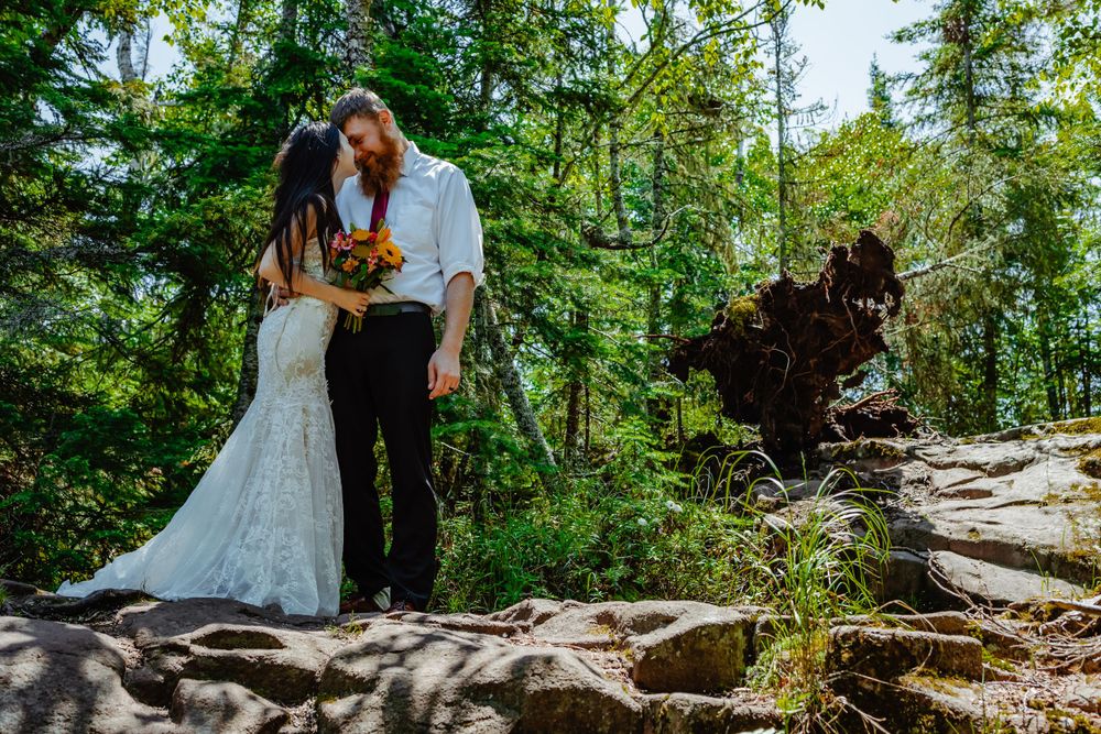 Romantic wedding portrait on rocky terrain surrounded by verdant forest landscape.
