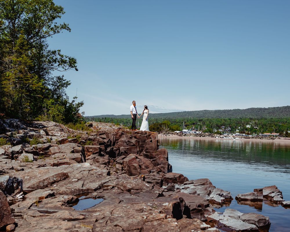 Wedding couple celebrating on rocky cliff overlooking scenic lake and forest vista.