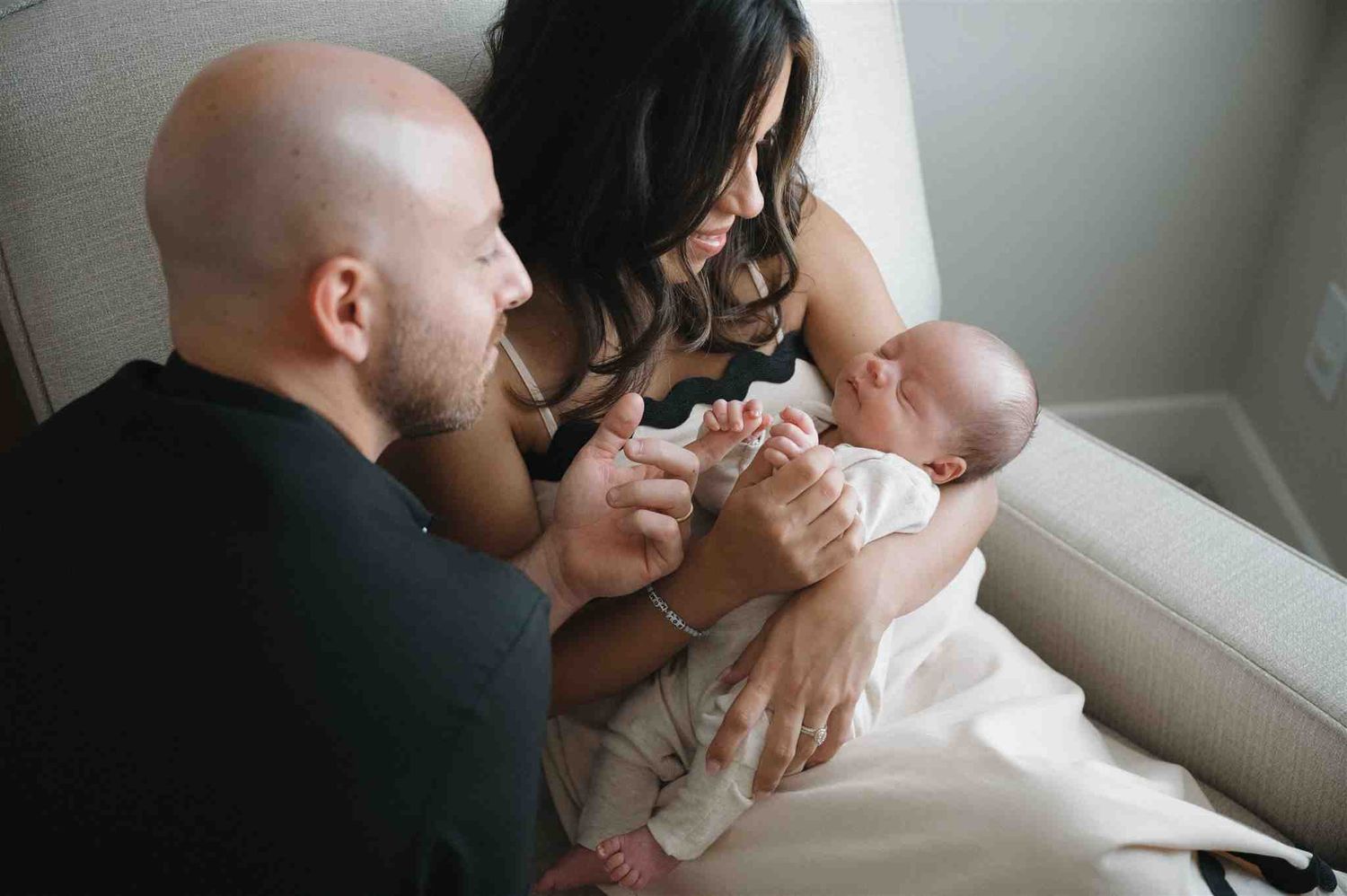 Parents spend a tender moment together feeding their newborn baby by a window.