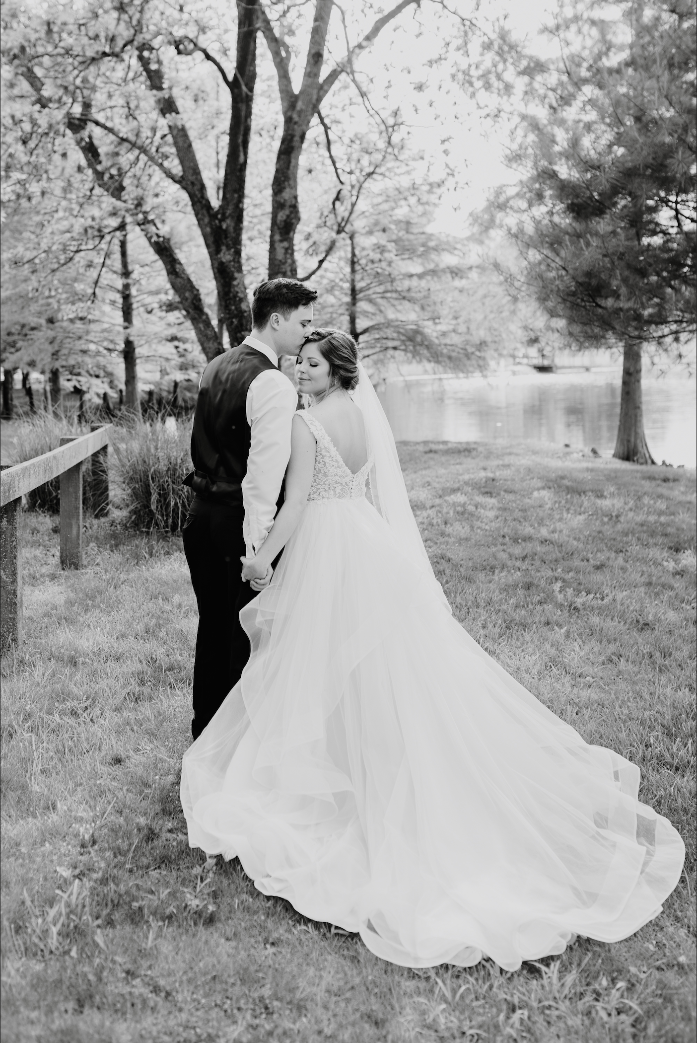 Black and white wedding portrait by lake with bride's dress flowing in elegant pose.