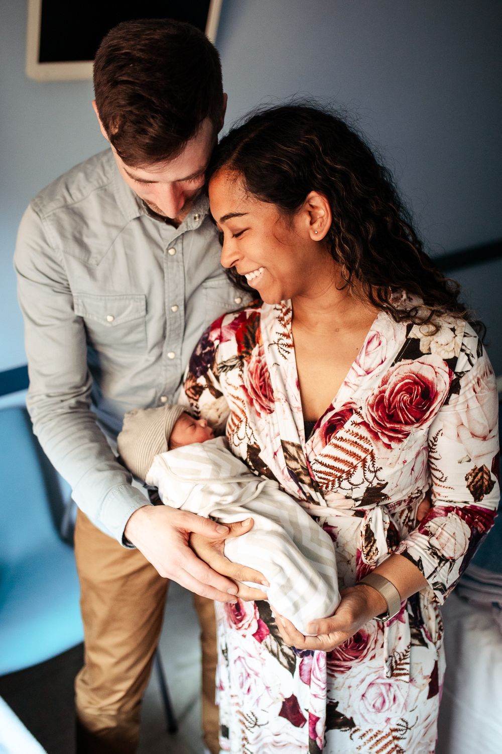 Parents sharing tender moment with newborn baby against blue wall.