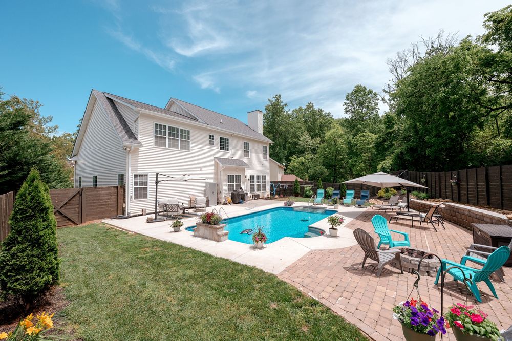 Sunny backyard with pool, brick patio, and green lawn surrounded by privacy fencing.