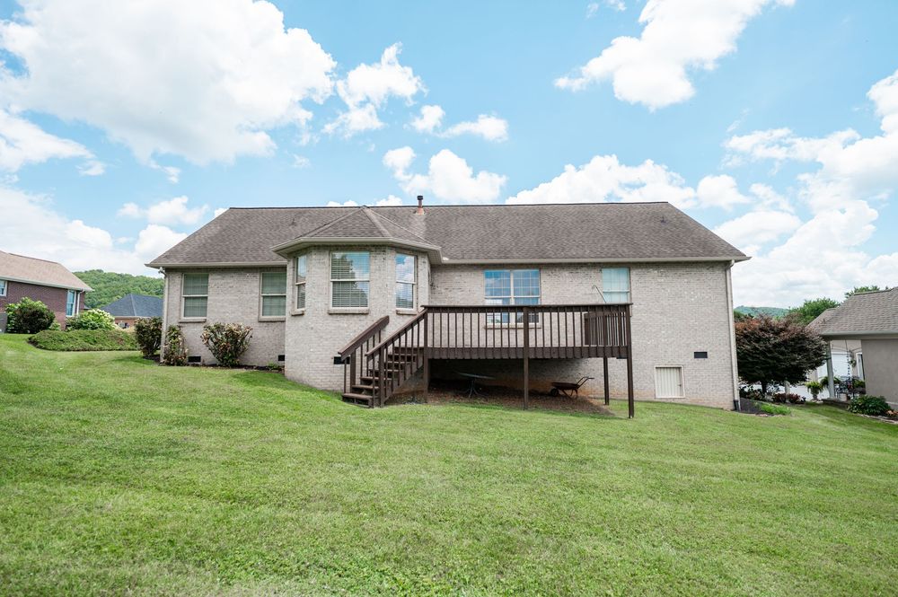A panoramic view of a residential backyard with green grass, wooden deck, and blue sky with white clouds.
