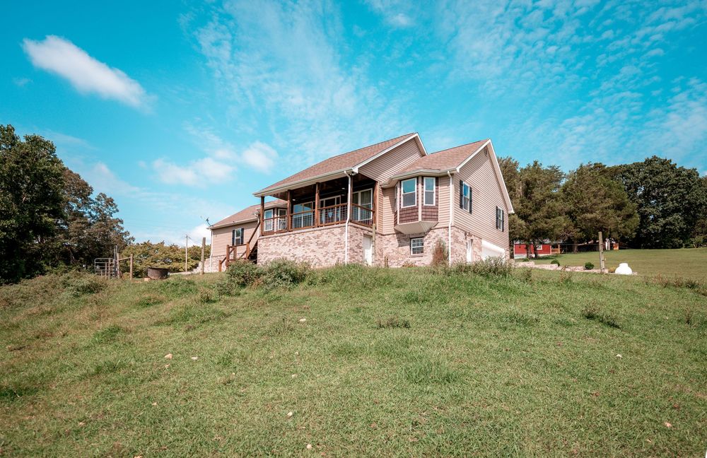 Panoramic view of a pink house on a grassy hillside with blue sky and scattered clouds above.