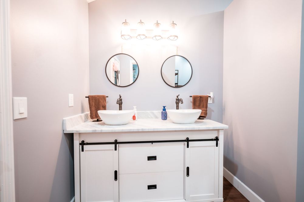 A modern white bathroom vanity with dual sinks, round mirrors, and wood accents creates a clean, minimalist design.