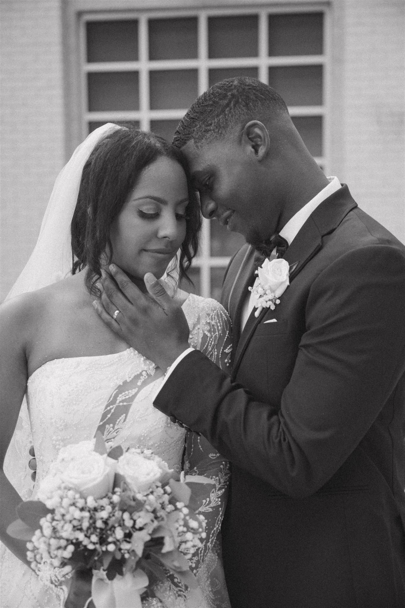 Black and white wedding portrait of newlyweds sharing an intimate moment outdoors in formal attire.