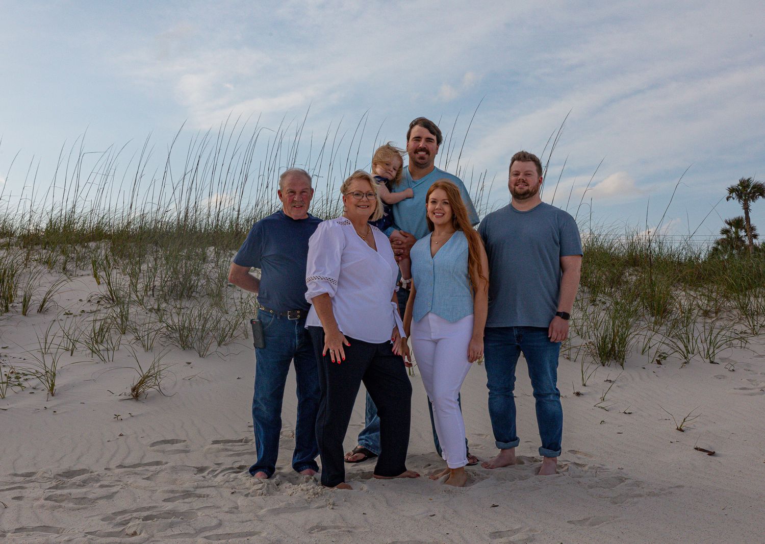 Multi-generational family group posing together on sand dunes at beach.