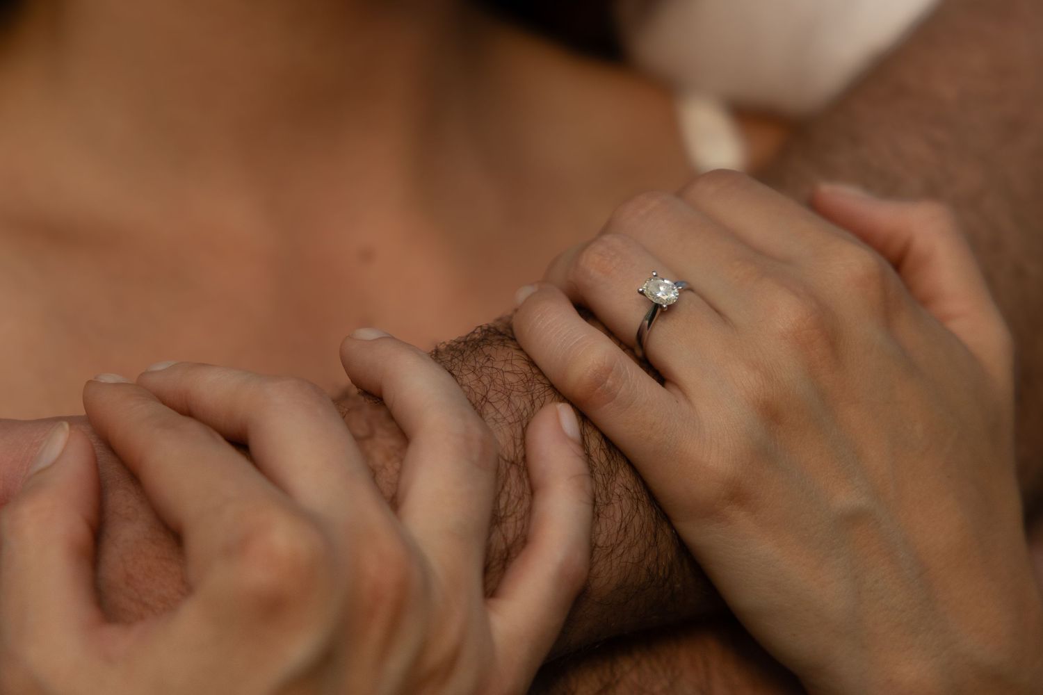 Close-up of hands with engagement ring in romantic setting.