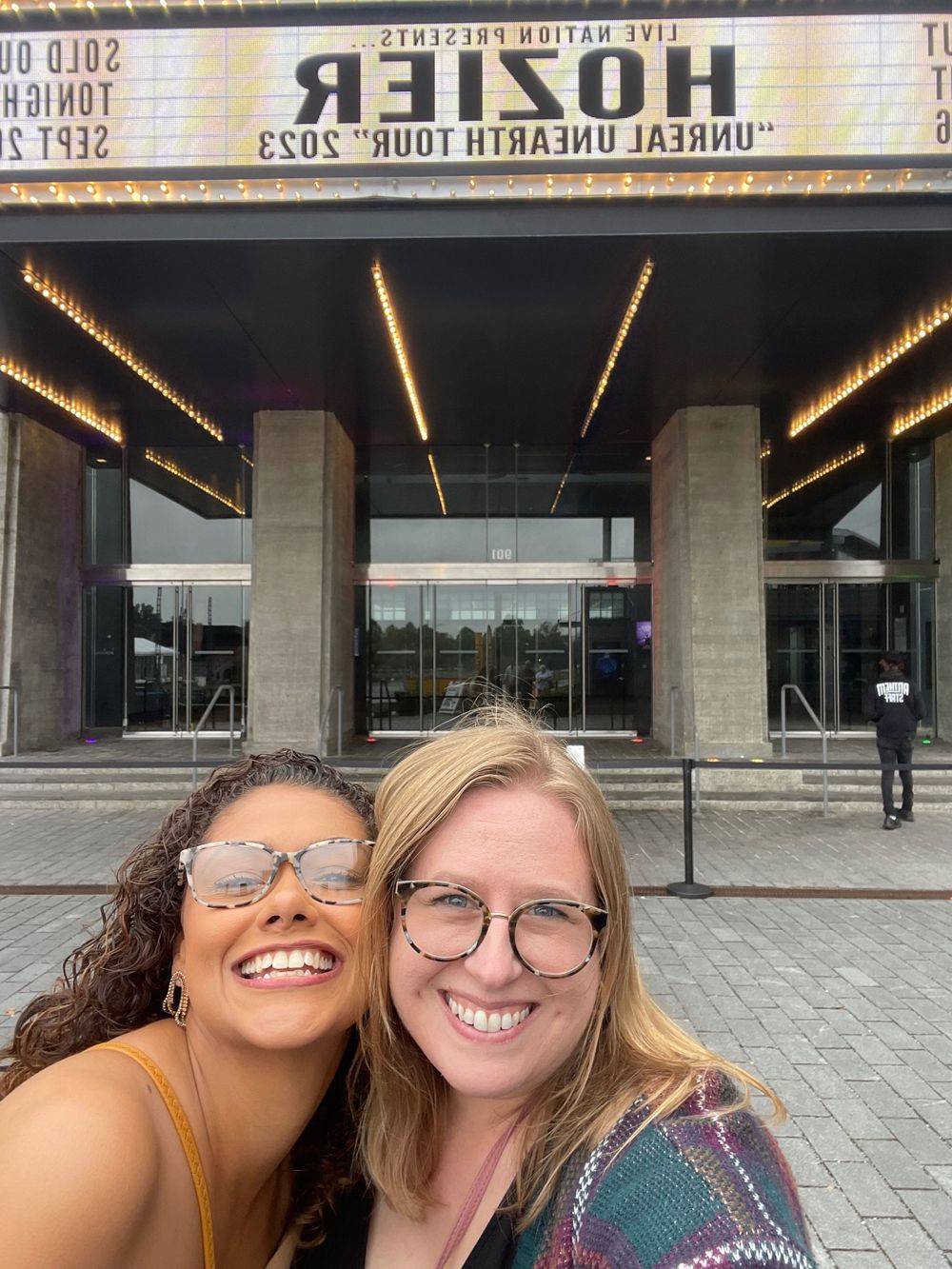 Two friends laughing together while taking selfies outside a building.