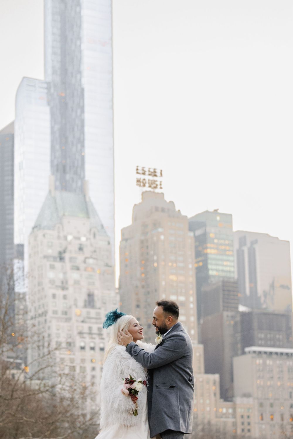A couple shares a romantic moment in front of the New York City skyline on an overcast winter day.