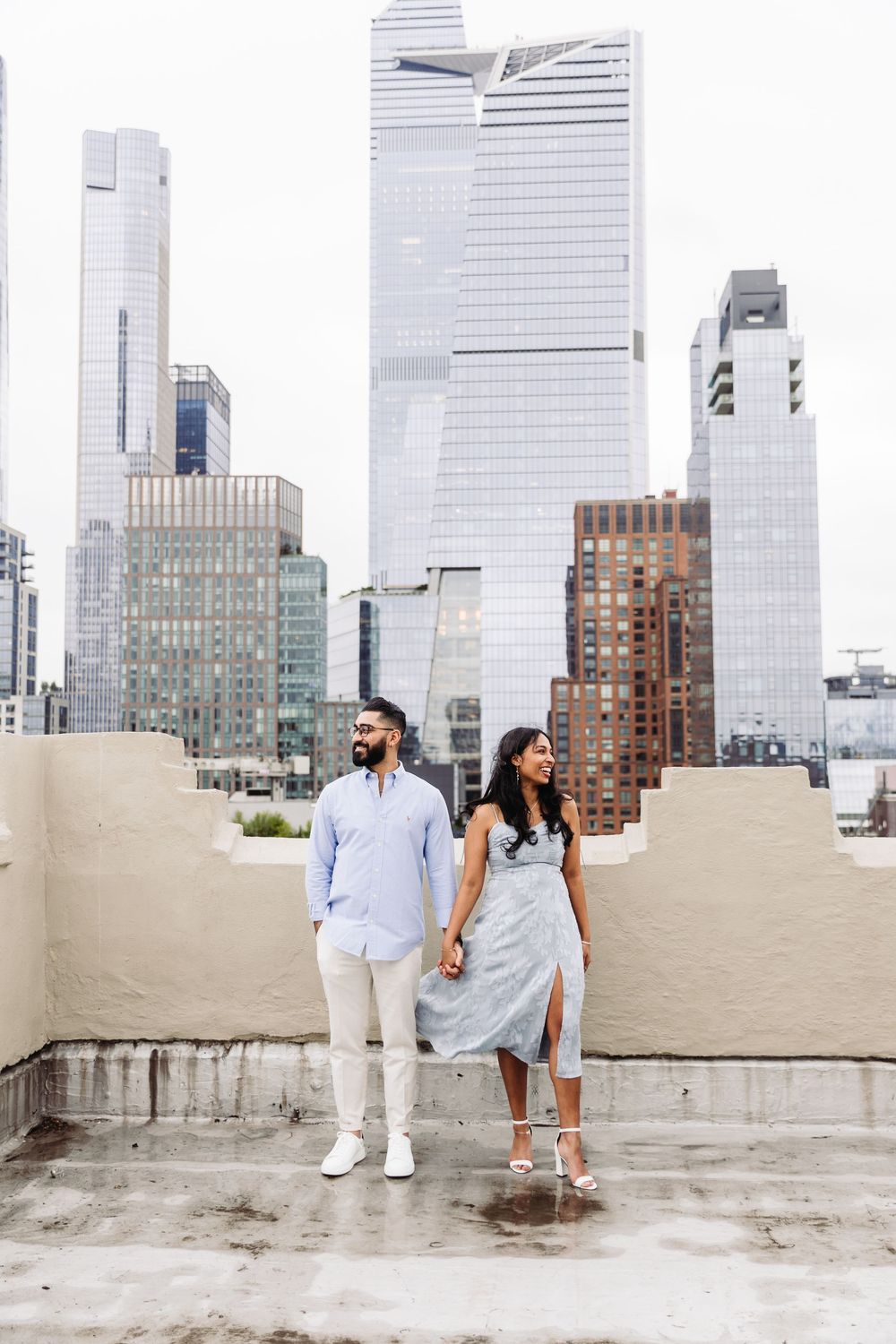 Stylish couple poses on rooftop with modern Hudson Yards buildings in background.
